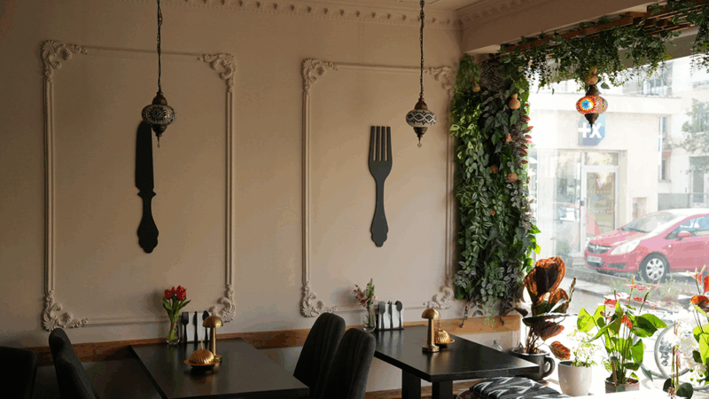 Vue d'ensemble sur les tables du restaurant décoré d'éléments ouïghours ainsi que de plantes vertes