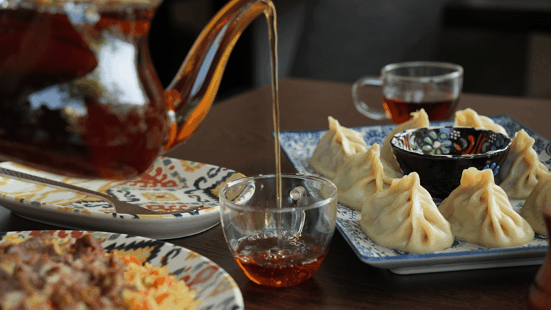Théière versant du thé dans une tasse entourée de plats ouïghours